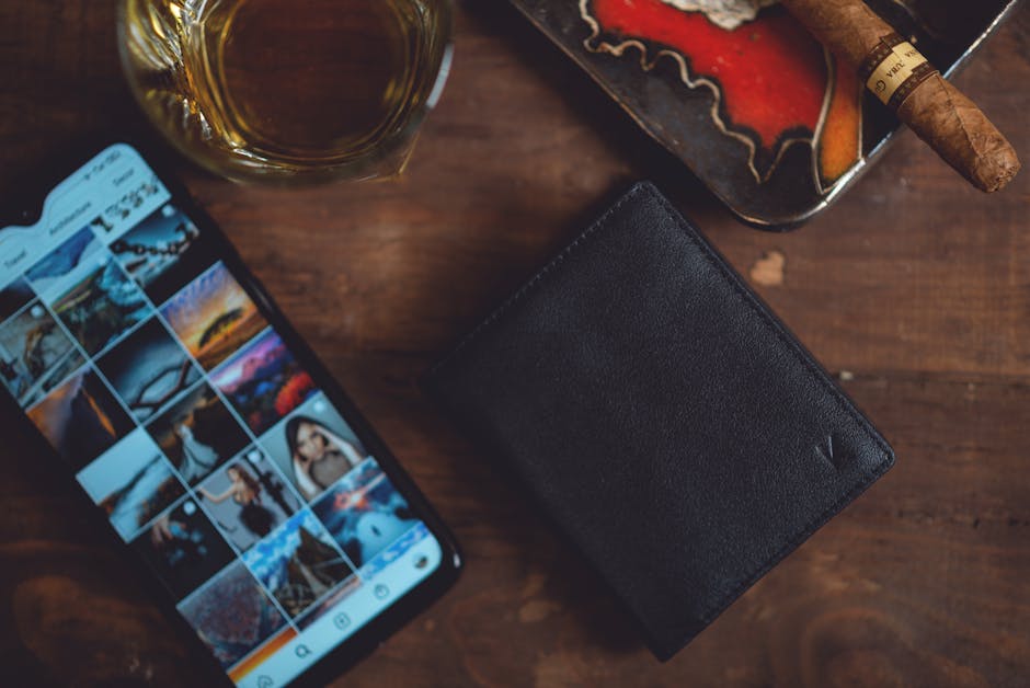 Elegant arrangement featuring a leather wallet, smartphone, cigar, and whiskey on a wooden table.